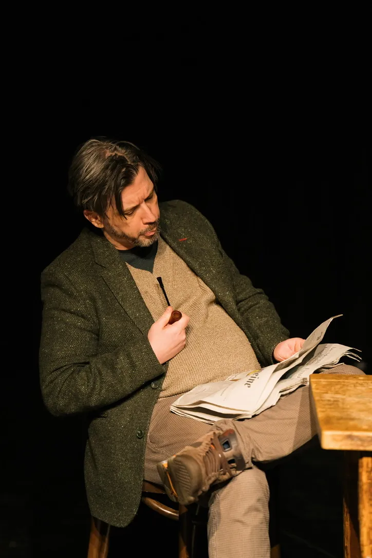 On stage, reading the paper with a pipe